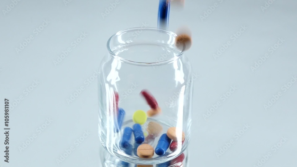 Colorful pills fall down into a bottle, on white, reflection, slow motion