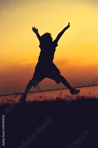 Silhouette of child jumping against sunset. Boy enjoying the view at riverside