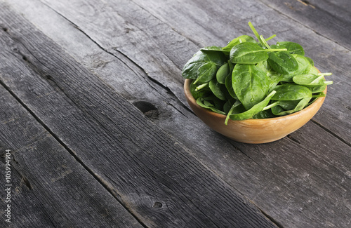 Spinach leaves in bowl on dark wooden background
