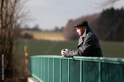 Elderly man praying at the handrail of a bridge