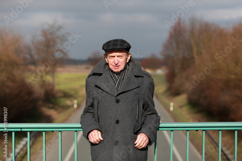Elderly man standing at the handrail of a bridge