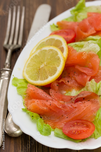 salad with smoked salmon on white dish on brown wooden background