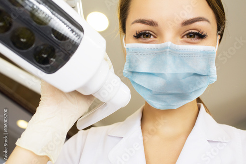 young women dentist with sterile mask readily approaching a patient with dental instruments held in the hands protected with surgical gloves young dentist with sterile mask photo