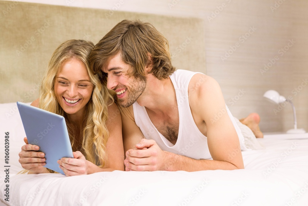 Obraz premium Cute couple using tablet lying in bed