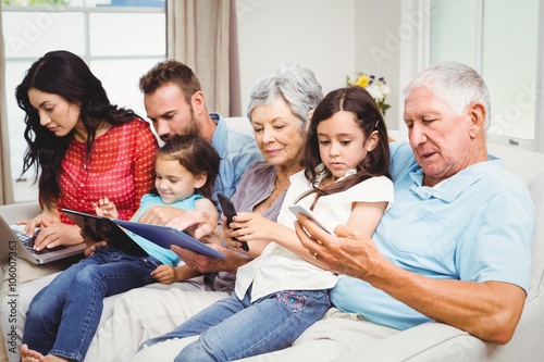 Family using technologies while sitting on sofa 