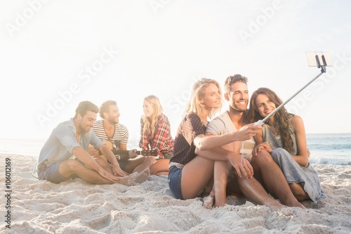 Smiling friends sitting on sand singing and taking selfies © WavebreakMediaMicro