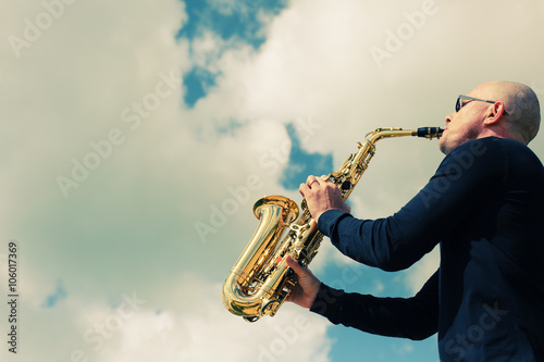 Canvas Print Saxophonist playing on saxophone on blue sky background