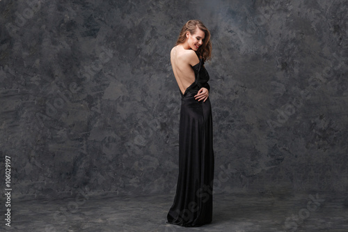 Happy seductive woman in long evening dress with open back
