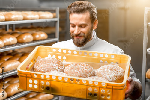 Handsome baker holding box full of freshly baked buckweat breads at the manufacturing