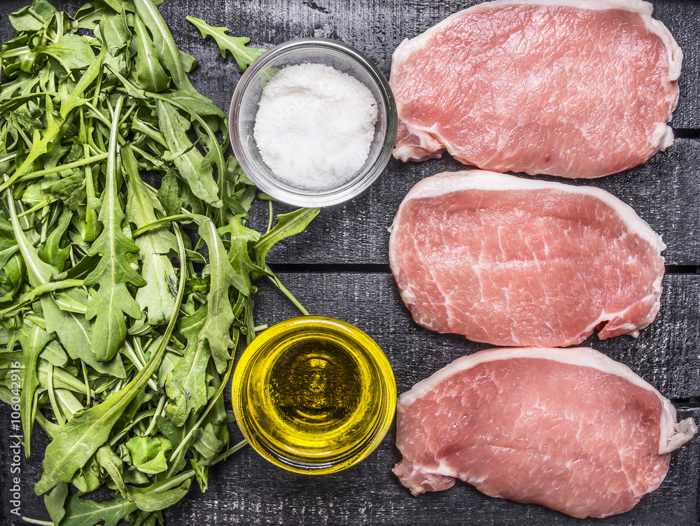 green salad of arugula with oil and salt with raw pork steak on wooden rustic background top view close up green salad of arugula with oil and salt with raw pork steak on wooden rustic background top view close up