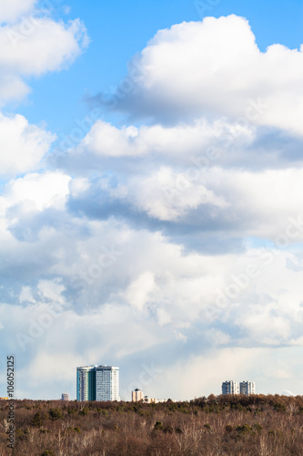 cumulus clouds in sky over buildings and woods