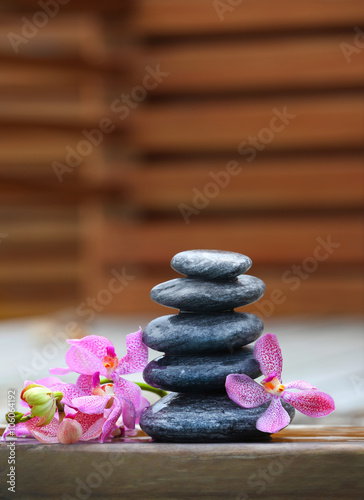 Stack of spa stones with pink orchids on wooden wet bridge