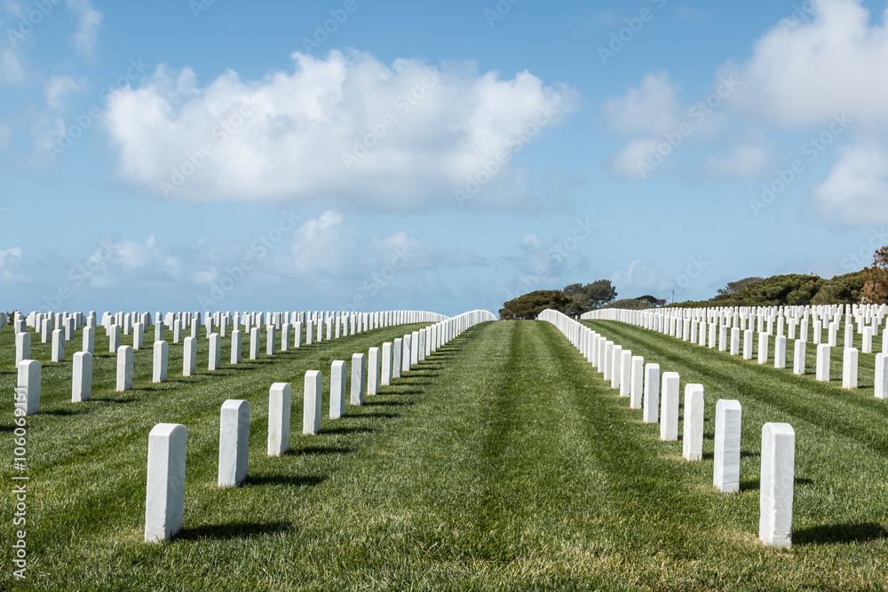 Grave markers in rows with a cloudy blue sky at Fort Rosecrans National Cemetery in San Diego, California. 
