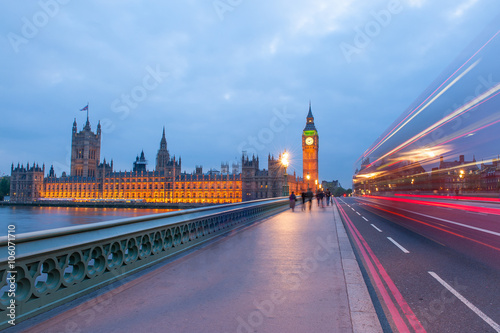 Traffic through London. Big Ben, one of the most prominent symbols of both London and England, as shown at night along with the lights of the cars and buses passing by.