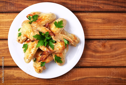 Plate with baked chicken wings and parsley on a wooden background photo
