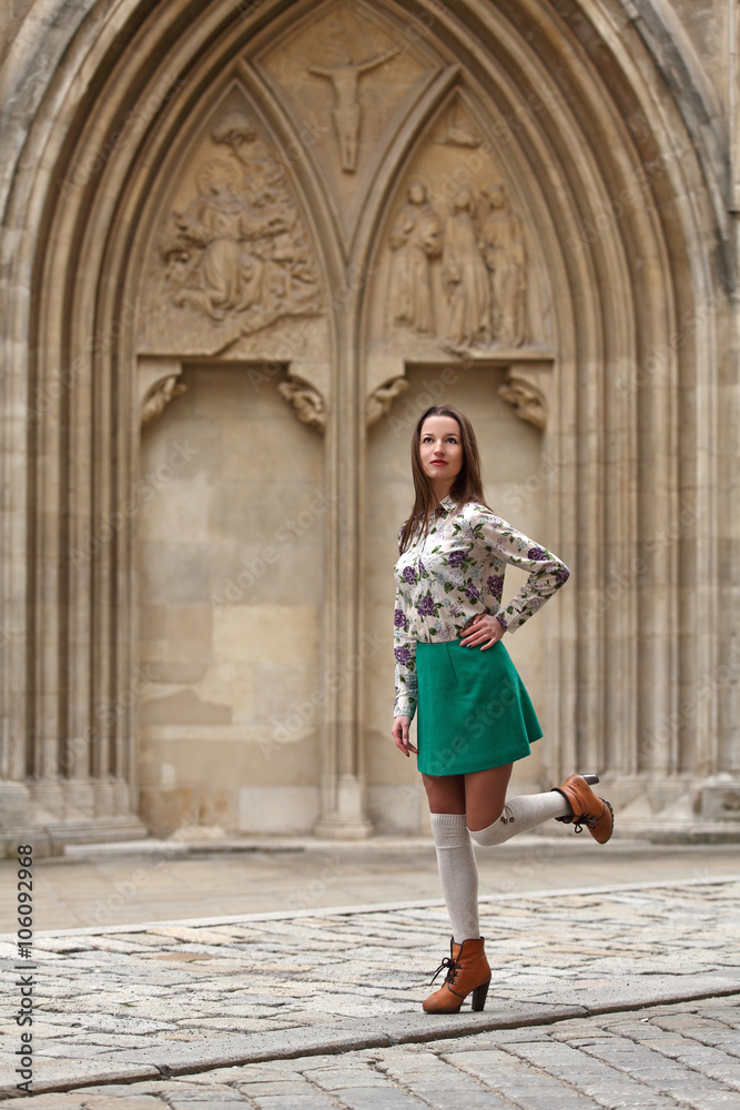 Young woman with turquoise skirt and white stockings in front of gothic architecture