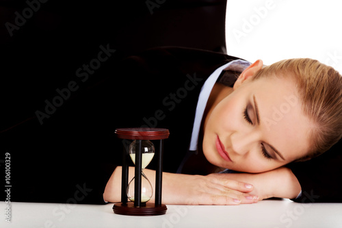 Young business woman sleeping on the desk with hourglass photo