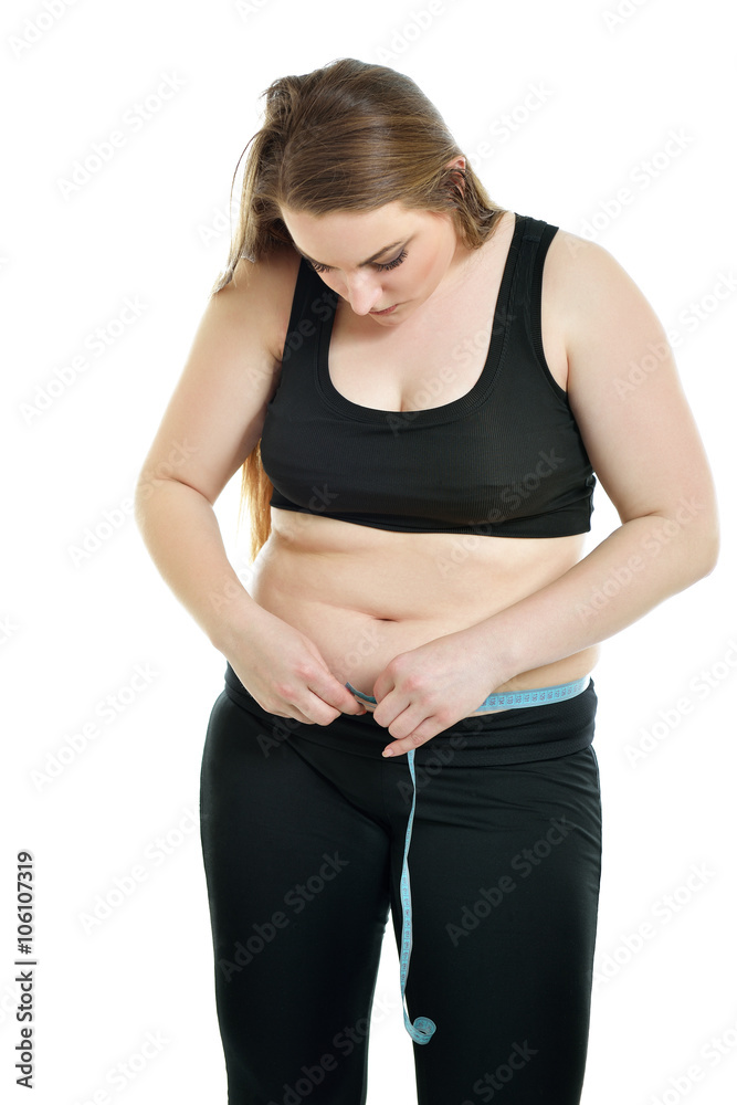 Overweight unhappy young woman measuring her belly over white ba