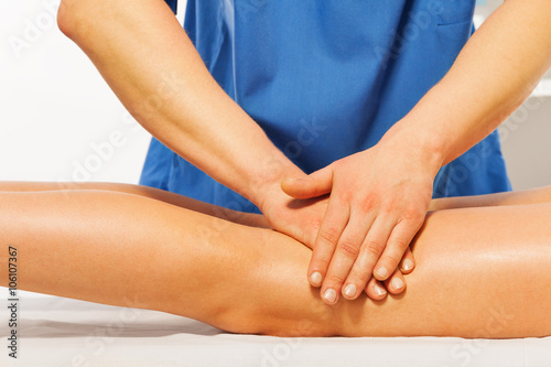 Close-up of masseur's hands kneading female leg