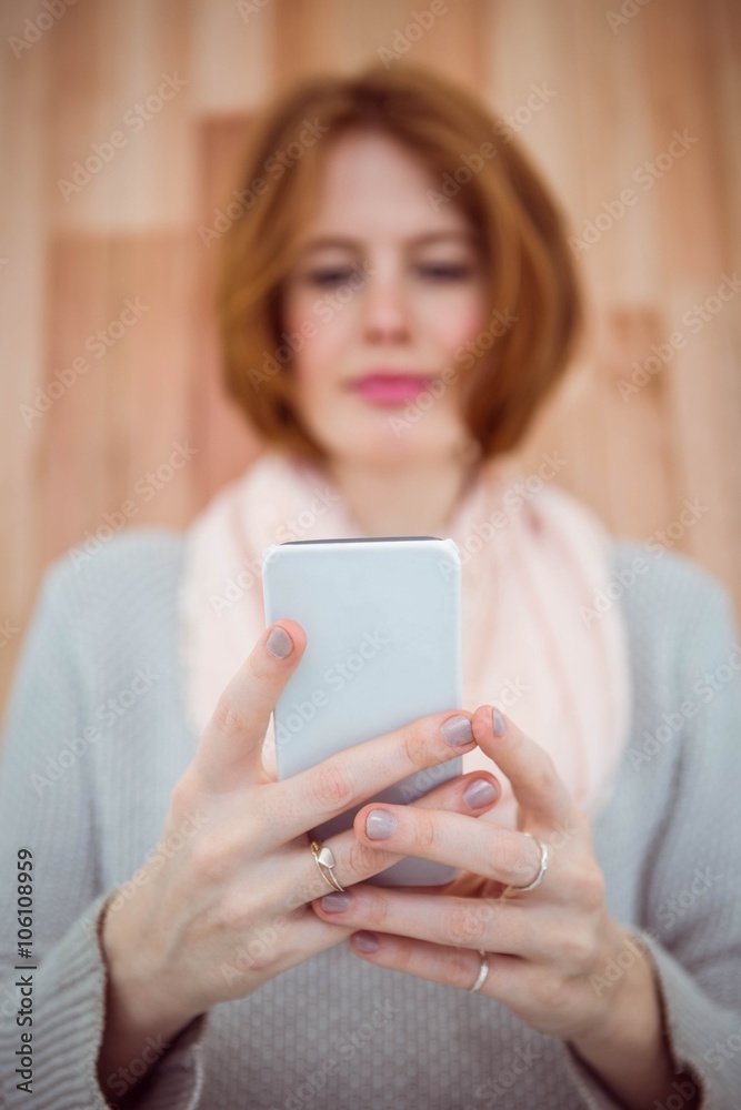 Red haired hipster using smartphone on wooden background