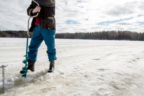 ice fisherman drills using a bore on the lake in winter on a sunny day in the woods