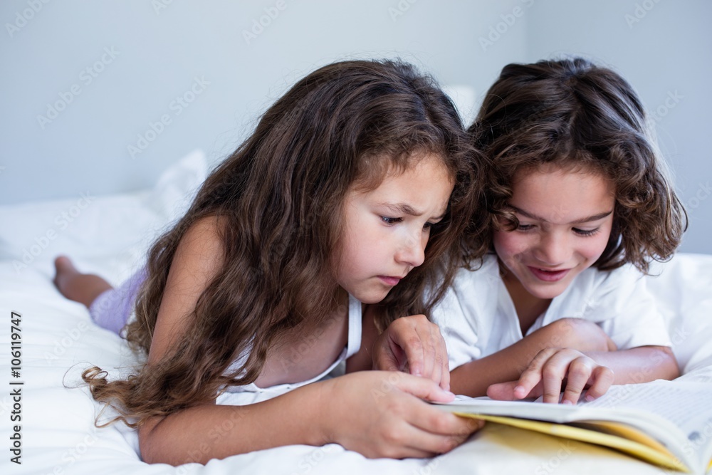 Brother and sister reading book together on bed Brother and sister reading book together on bed