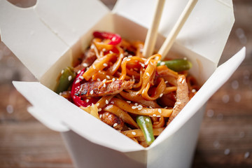 Noodles with pork and vegetables in take-out box on wooden table