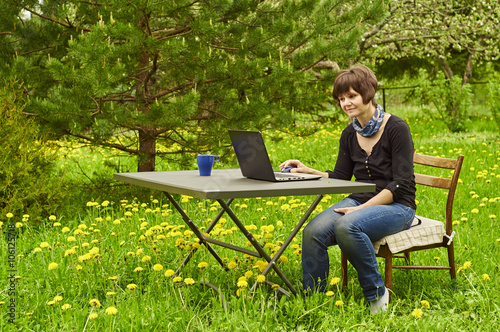 Middle aged woman working on laptop in blossoming garden photo