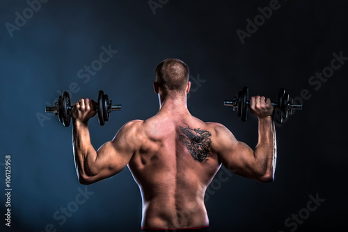 strong man bodybuilder lifting dumbbells on dark background back view