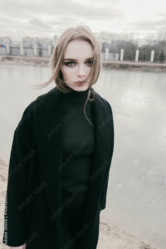 portrait of a beautiful young blonde woman in a black jacket on the street, cloudy