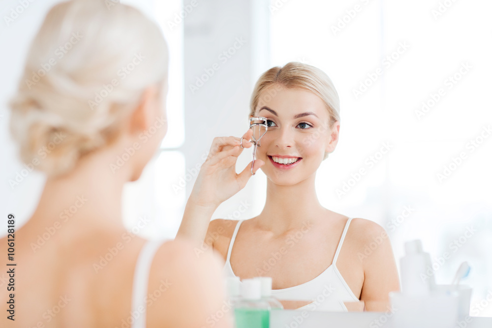 woman with curler curling eyelashes at bathroom woman with curler curling eyelashes at bathroom