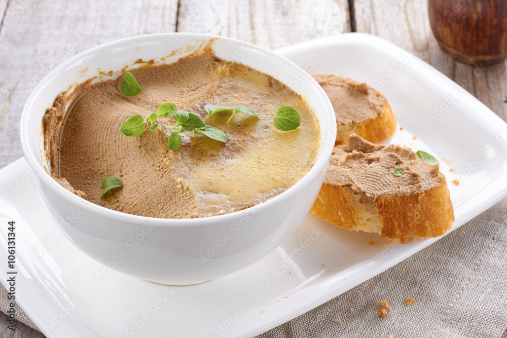 Homemade chicken liver pate on baquette and in white bowl Homemade chicken liver pate on baquette and in white bowl