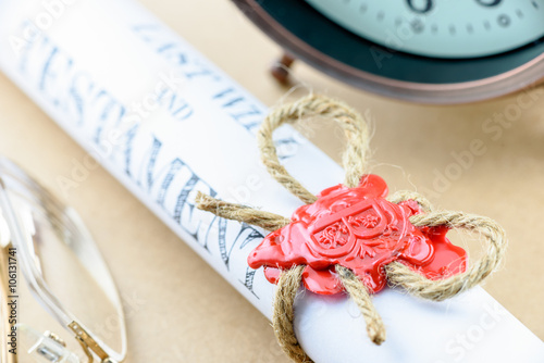 Rolled up scroll of last will and testament fastened with natural brown jute twine hemp rope, sealed with sealing wax and stamped with alphabet letter B. Decorated with an antique clock and glasses. photo