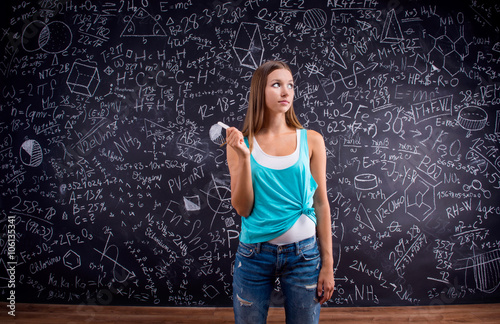 Thinking girl holding head against big blackboard, back view