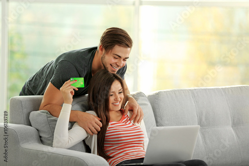 Young happy couple using credit card with laptop at home on light background