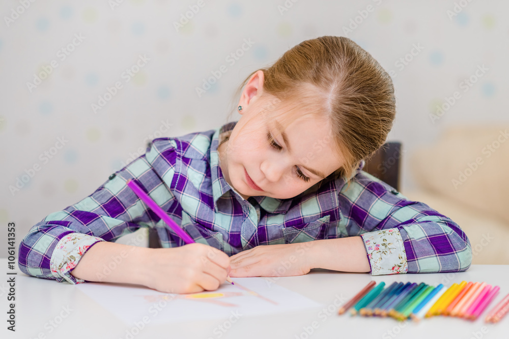 Beautiful pensive little girl with blond hair sitting at white table and drawing with multicolored pencils Beautiful pensive little girl with blond hair sitting at white table and drawing with multicolored pencils