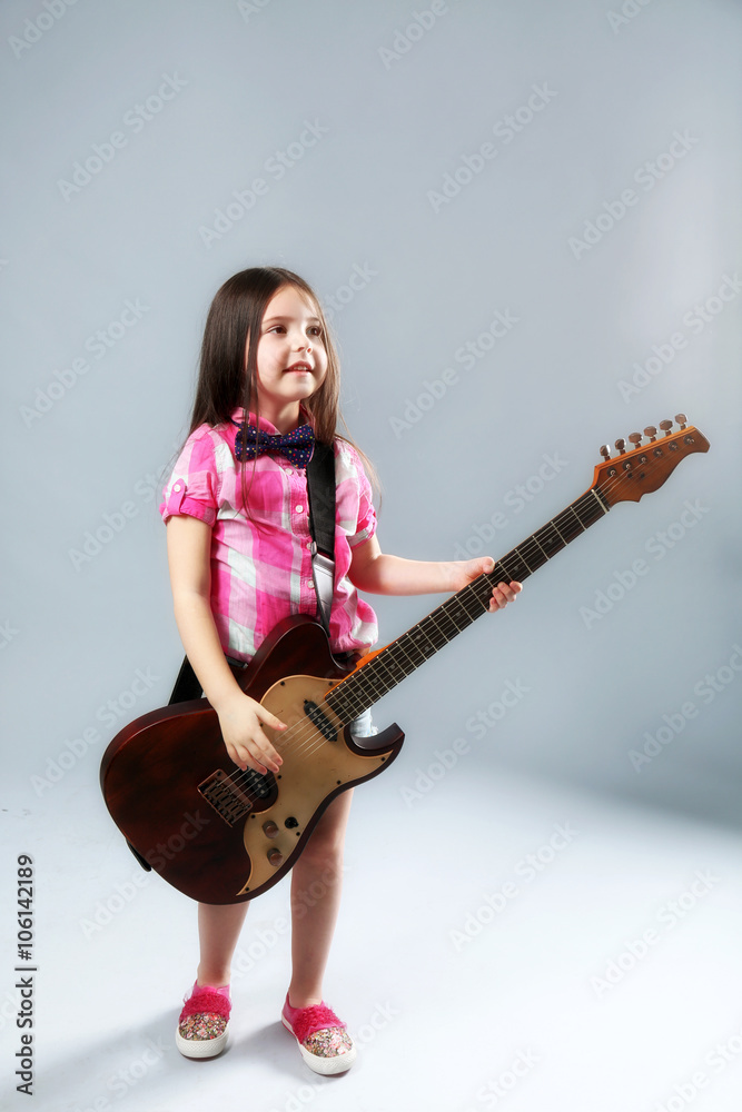 Beautiful artistic little girl playing guitar on grey background Beautiful artistic little girl playing guitar on grey background