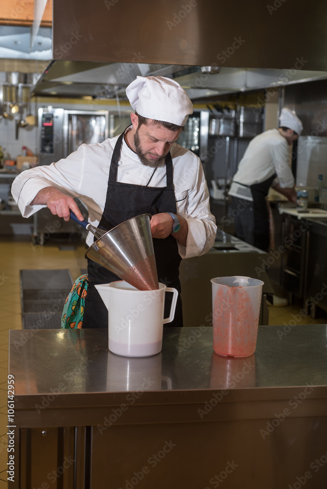 cook prepares a pureed strawberries through a strainer cook prepares a pureed strawberries through a strainer