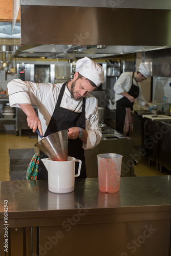 Fototapeta Naklejka Na Ścianę i Meble -  cook prepares a pureed strawberries through a strainer