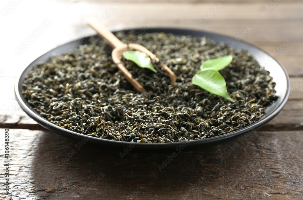 Dry tea with green leaves in black plate on wooden table background Dry tea with green leaves in black plate on wooden table background