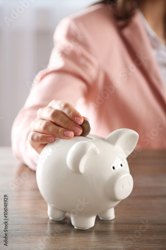 Woman putting coin into piggy bank at the table