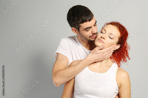 Happy young couple in love embracing on grey background