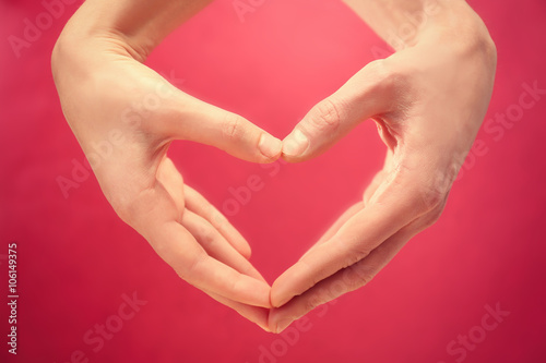 Male and female hands making heart with fingers on red background