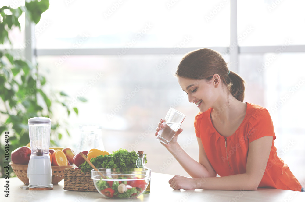 Young woman drinking water near table with fruits and vegetables in the kitchen Young woman drinking water near table with fruits and vegetables in the kitchen
