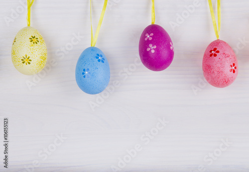 Colorful Easter eggs hanging on white wooden background