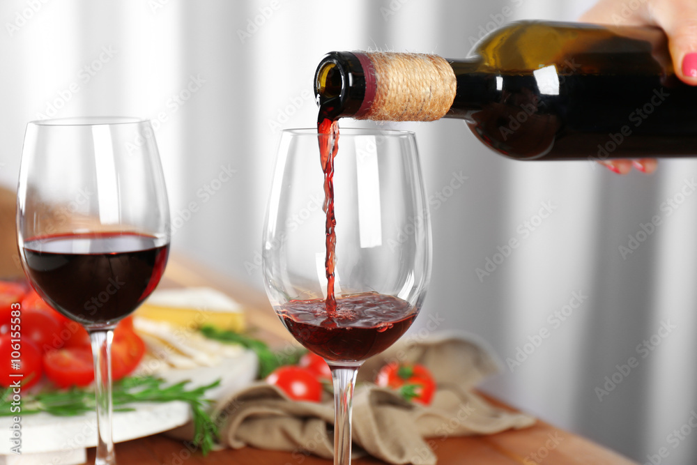 Pouring red wine into glass and food on wooden table closeup