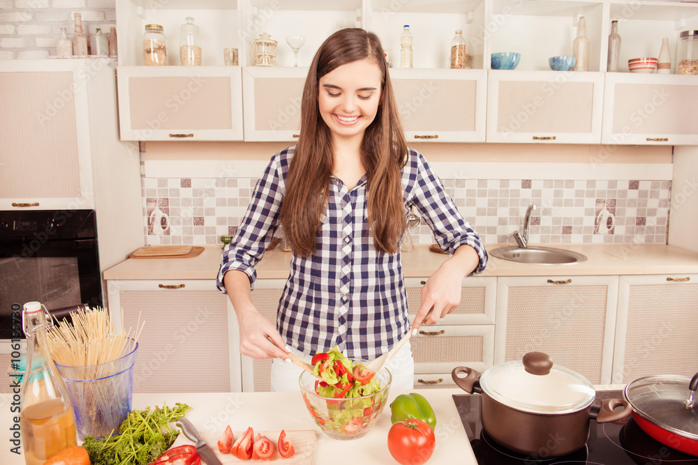 Attractive happy young girl mixing salad in the kitchen Attractive happy young girl mixing salad in the kitchen