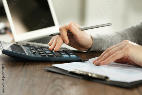Female hand holding a pen and using calculator while filling in the individual income tax return, close up