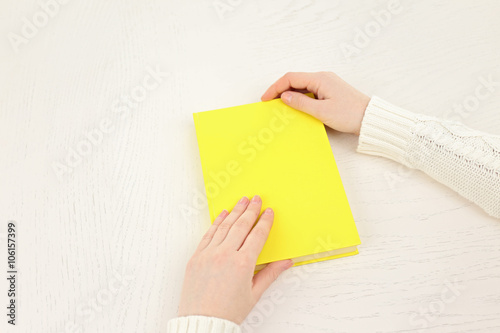 Female hands holding a yellow book cover  on white desk, top view