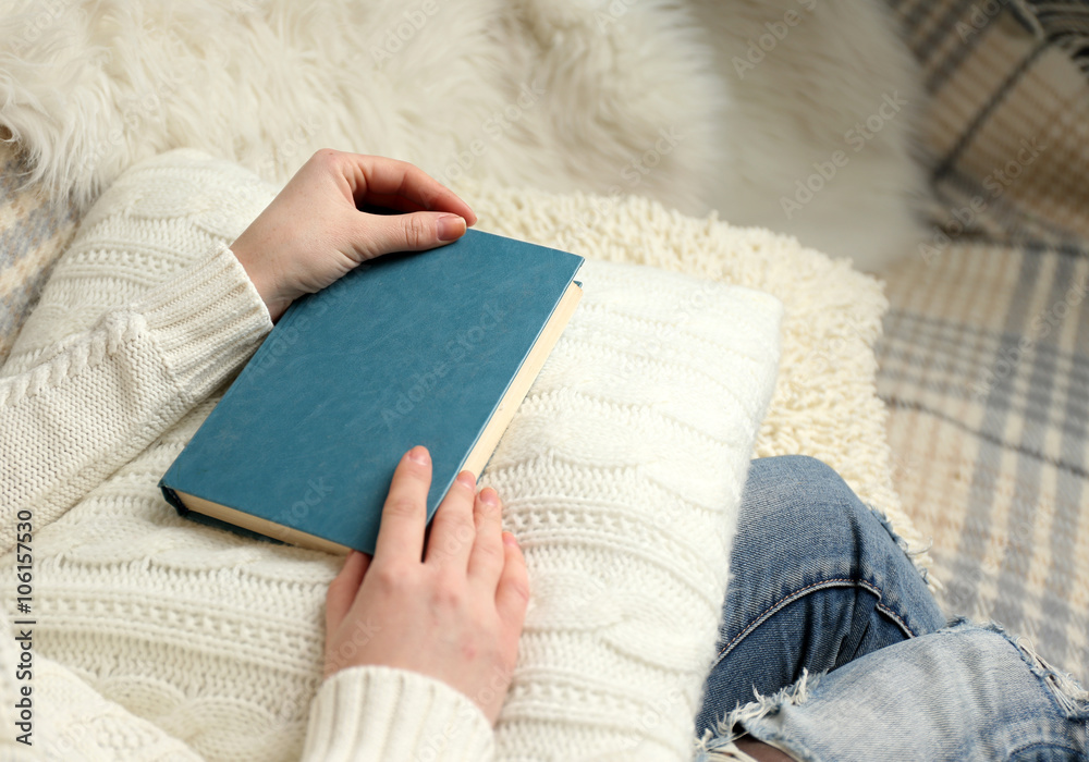 Obraz premium Young woman sitting on the sofa and holding a light-blue book cover on a white cushion, close up